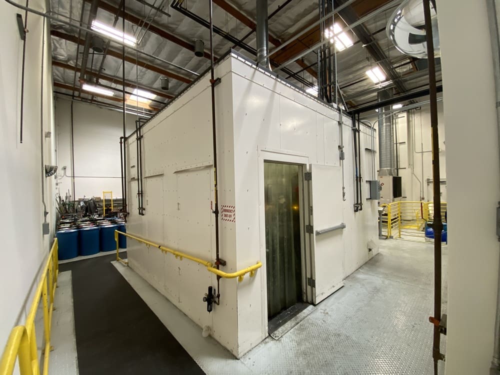 Large enclosed process unit with piping and guardrails inside an industrial facility