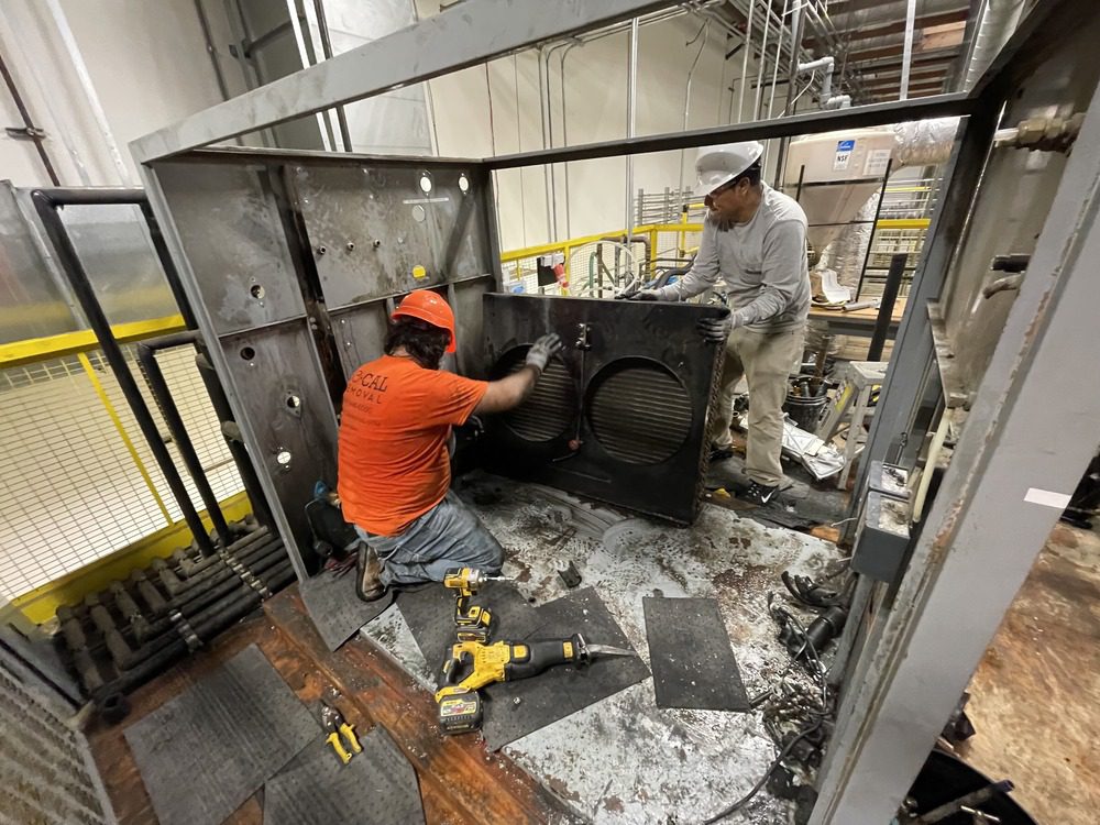 Workers separating panels from industrial equipment inside a facility