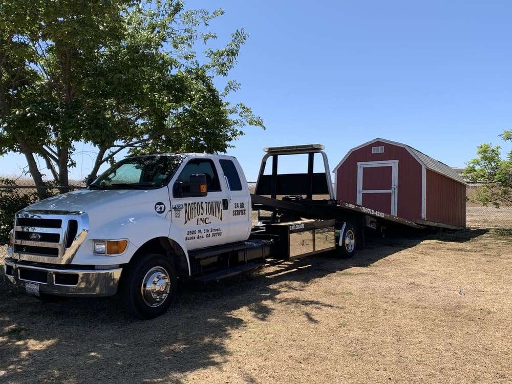 Tow truck transporting a small red storage structure.