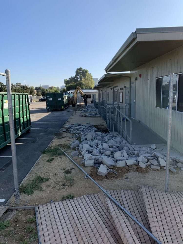 Broken concrete lined along modular-building ramps with an excavator in the distance.