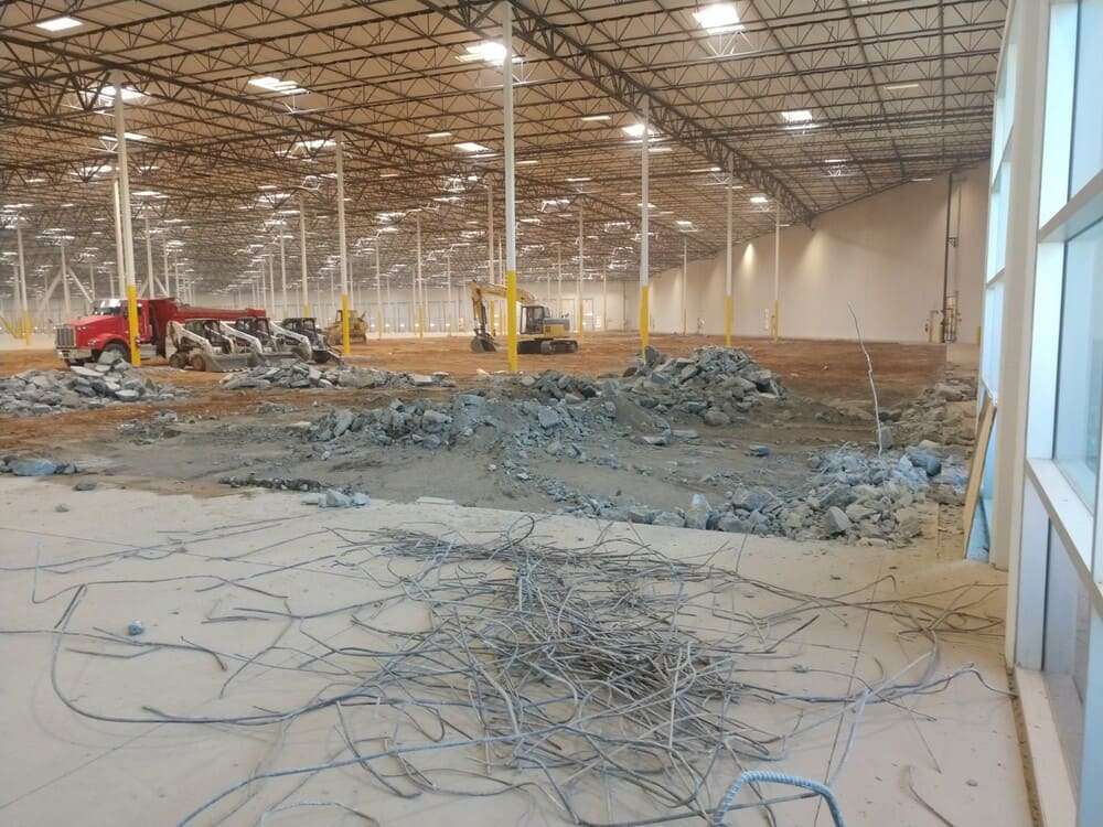 Interior commercial work area with broken concrete, exposed reinforcing steel and compact demolition equipment