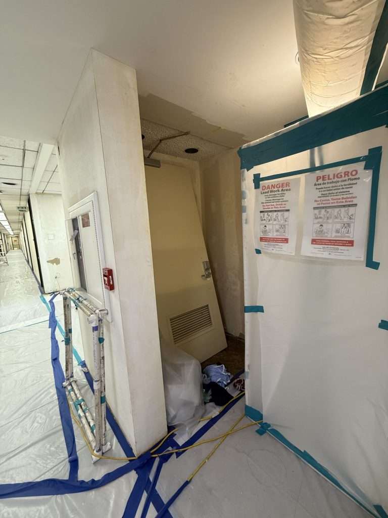 Sheeted interior work area with bilingual lead-work warning signs and protected flooring