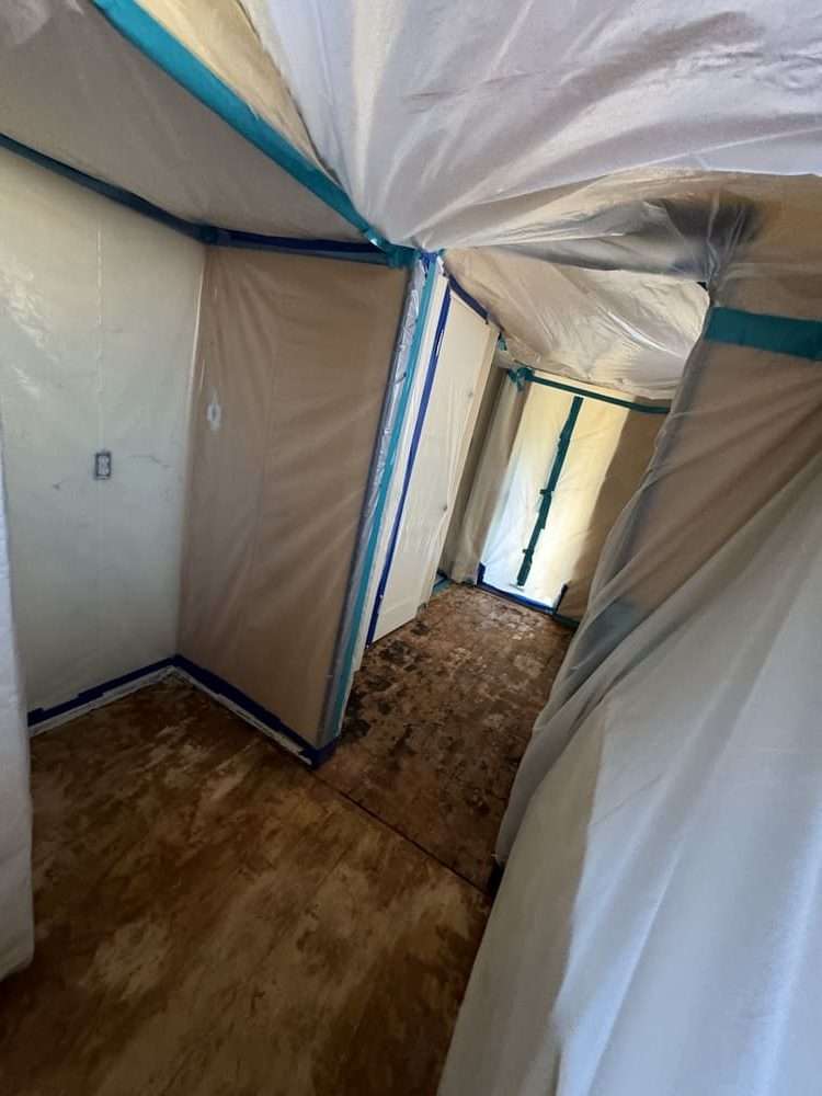 Interior corridor protected with plastic sheeting and taped barriers over exposed subfloor.
