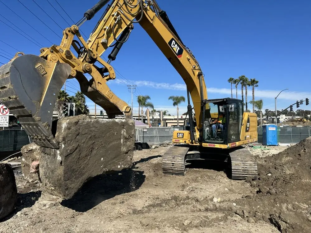 Excavator lifting broken concrete out of a Southern California removal site