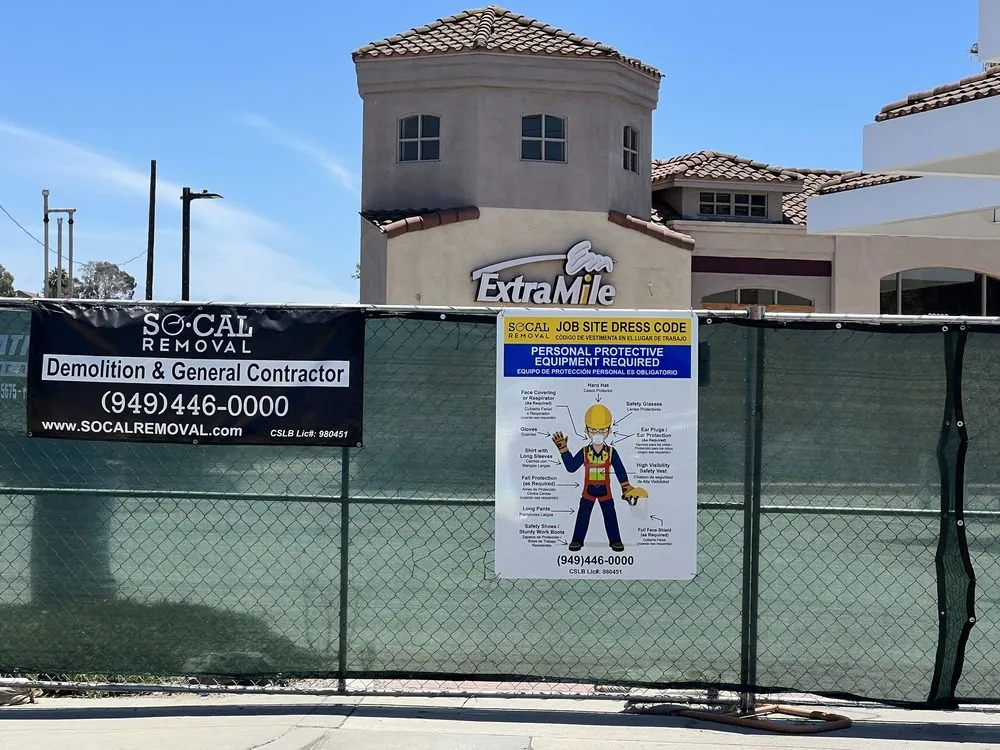 Screened perimeter fence with SoCal Removal contractor and PPE signage along a public sidewalk