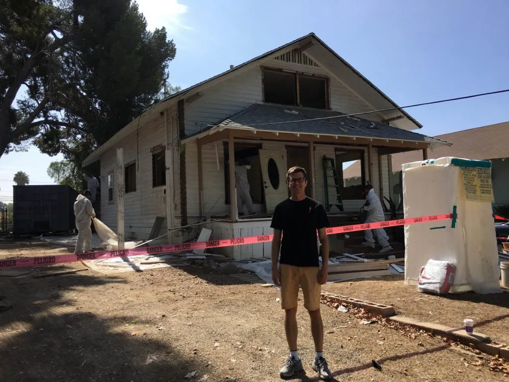 People in protective clothing working around a painted residential building behind a marked work boundary