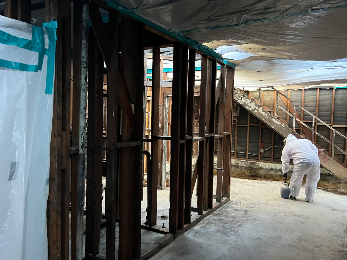 Worker in disposable coveralls applying amended water inside a sealed asbestos containment