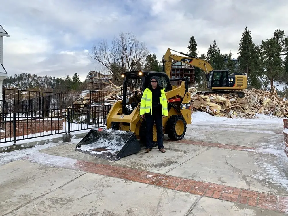 Worker standing between compact equipment and an excavator at a demolition site
