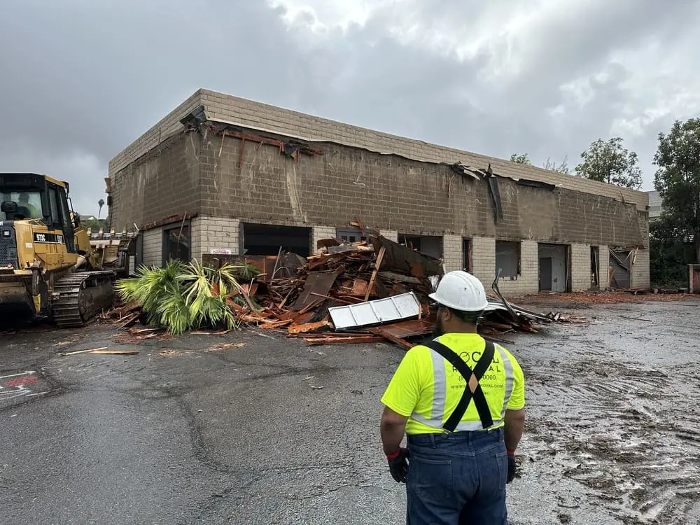 Worker observing a partially demolished commercial structure and debris pile