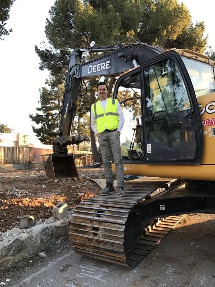 Andre Abajian beside a tracked excavator at a structure-removal site
