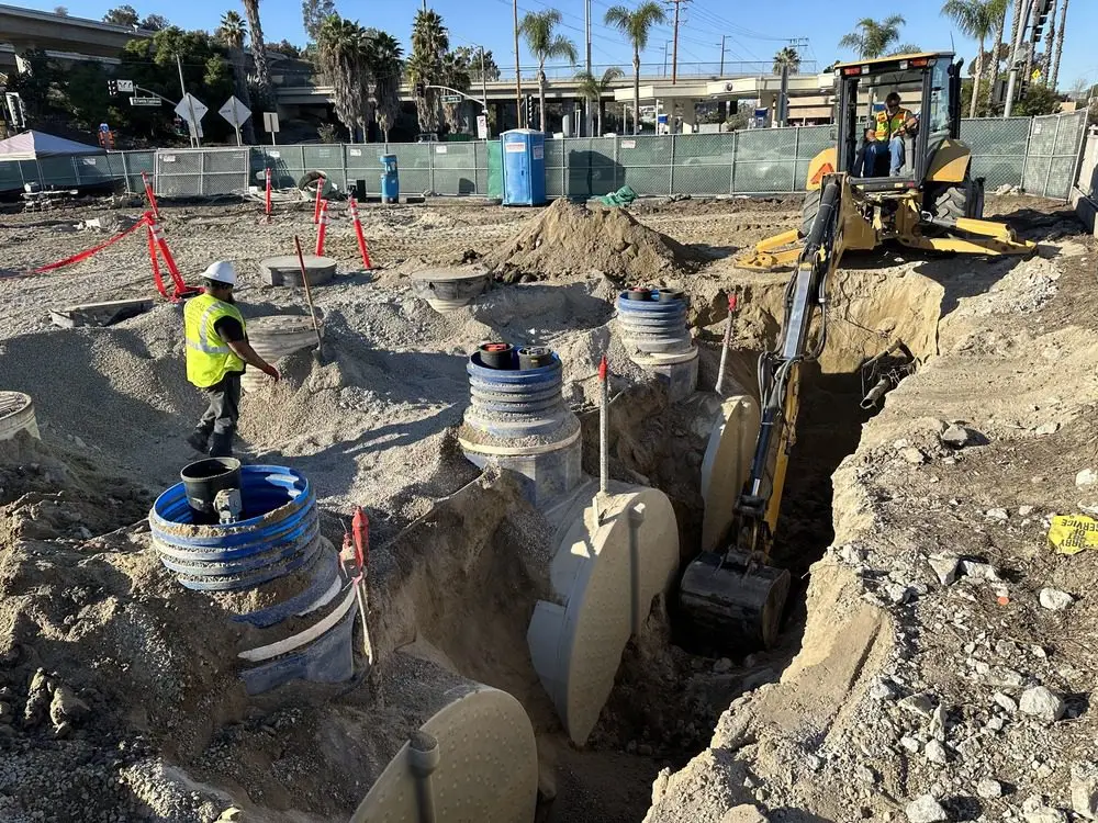 Excavator working in a trench between utility structures at an active project site