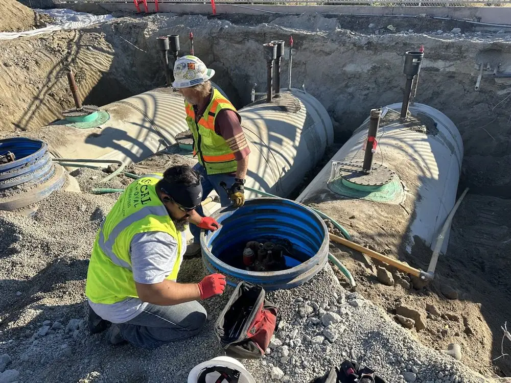 Two workers beside exposed underground storage tanks and piping in an excavation